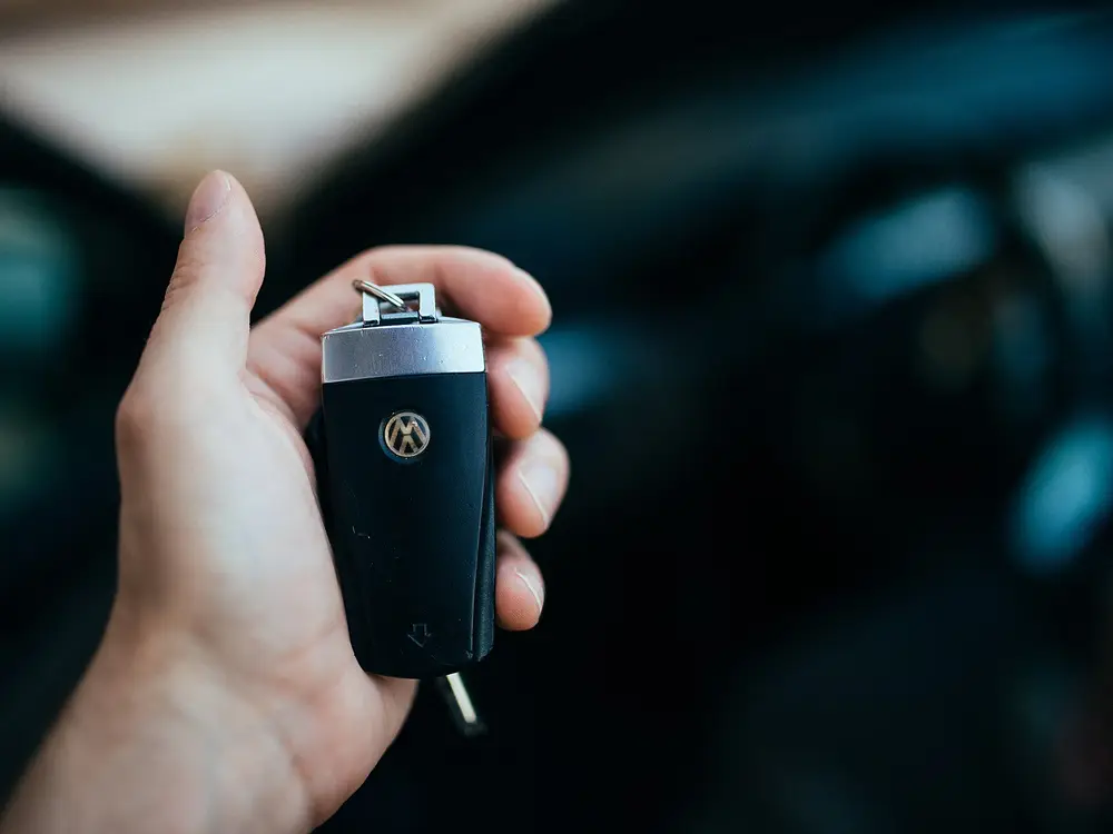 Hand holding a car key in front of a car