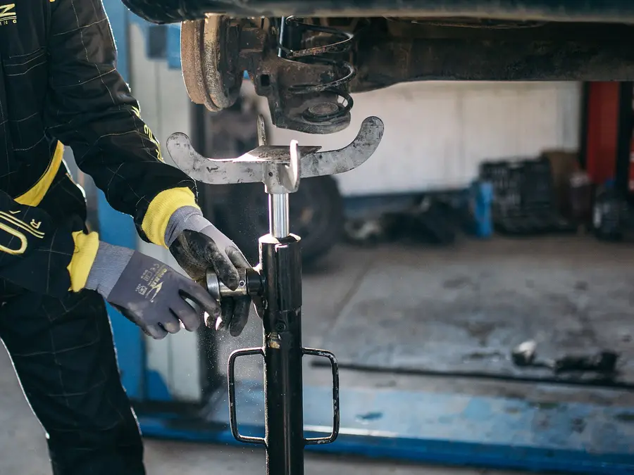 Mechanic working under a car on a lift, checking the front suspension