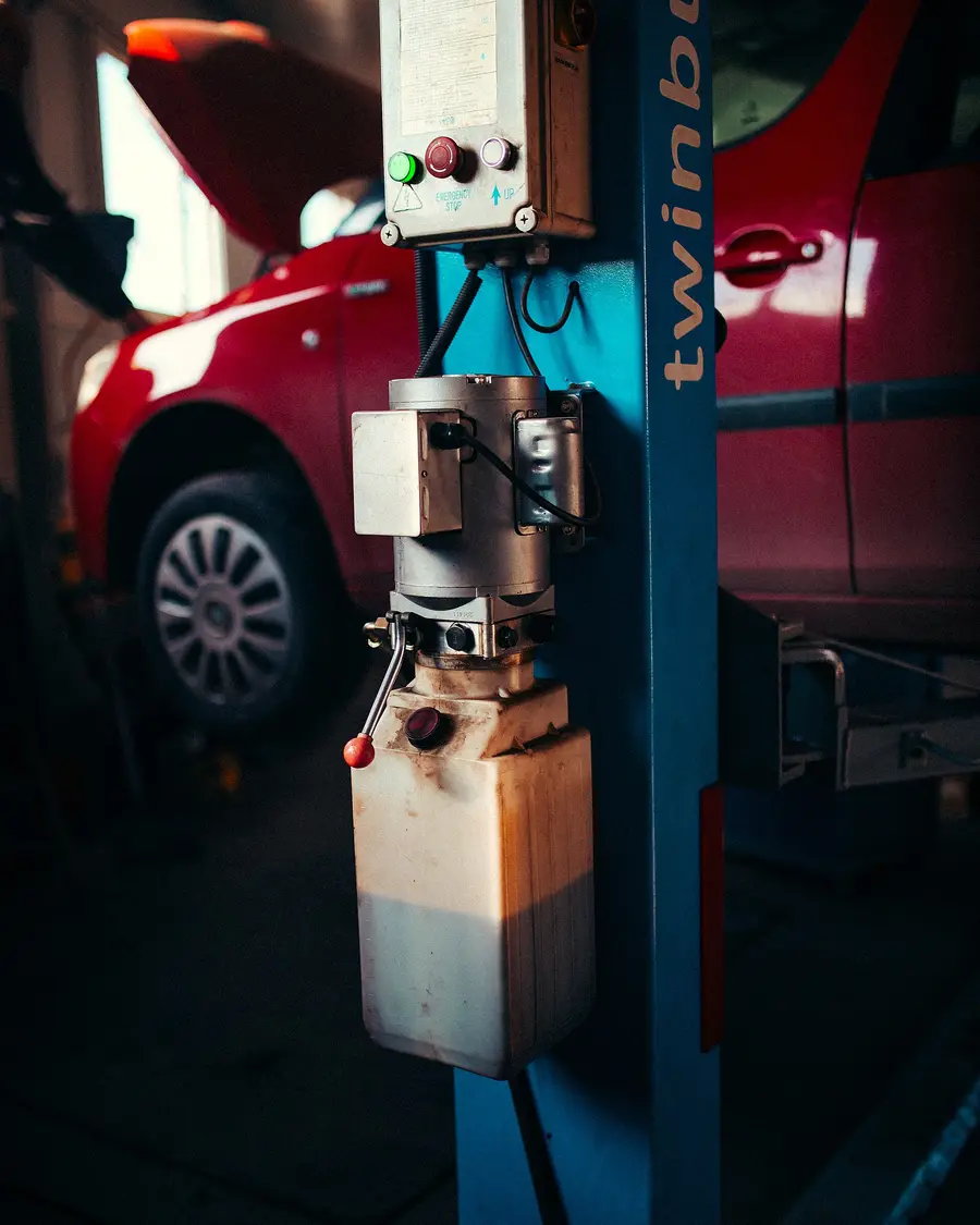 Hydraulic lift in a workshop with a red car raised behind it